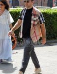 Men's summer coordinate and outfit with plain silver/black sunglasses, plain black t-shirt, beige/multi-colored check shirt, plain gray slacks, and beige Asics sneakers.