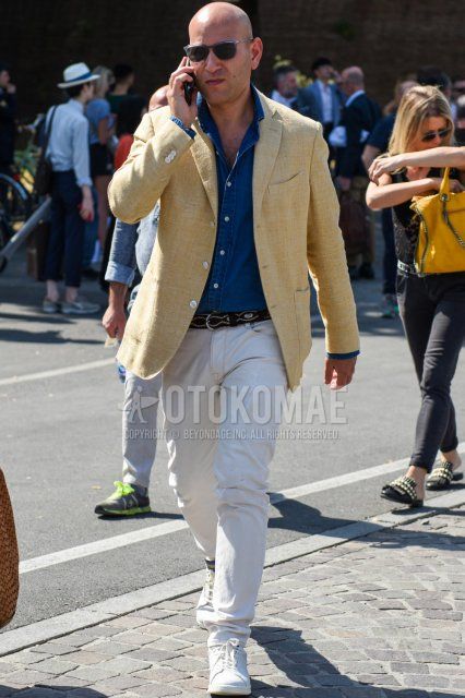 Men's spring/summer/fall outfit with solid black sunglasses, solid yellow tailored jacket, solid navy denim/chambray shirt, solid black leather belt, solid white cotton pants, and white low-cut sneakers.
