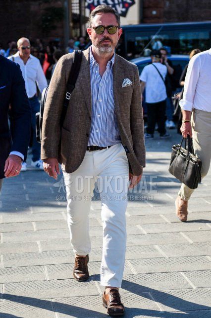 Men's spring and fall outfit with brown tortoiseshell sunglasses, plain brown tailored jacket, white/blue striped shirt, plain black mesh belt, plain white cotton pants, plain ankle pants, brown/beige wingtip leather shoes.