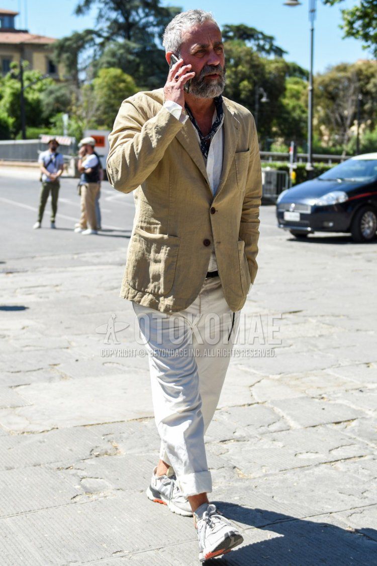 Men's spring, summer, and fall outfit with navy stole bandana/neckerchief, plain beige tailored jacket, plain white shirt with band collar, plain white cotton pants, and Adidas gray low-cut sneakers.