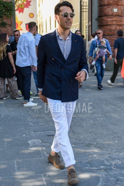 Men's spring, summer, and fall coordination and outfit with clear/black solid sunglasses, navy solid tailored jacket, white/navy striped shirt, white solid cotton pants, and brown low-cut sneakers.