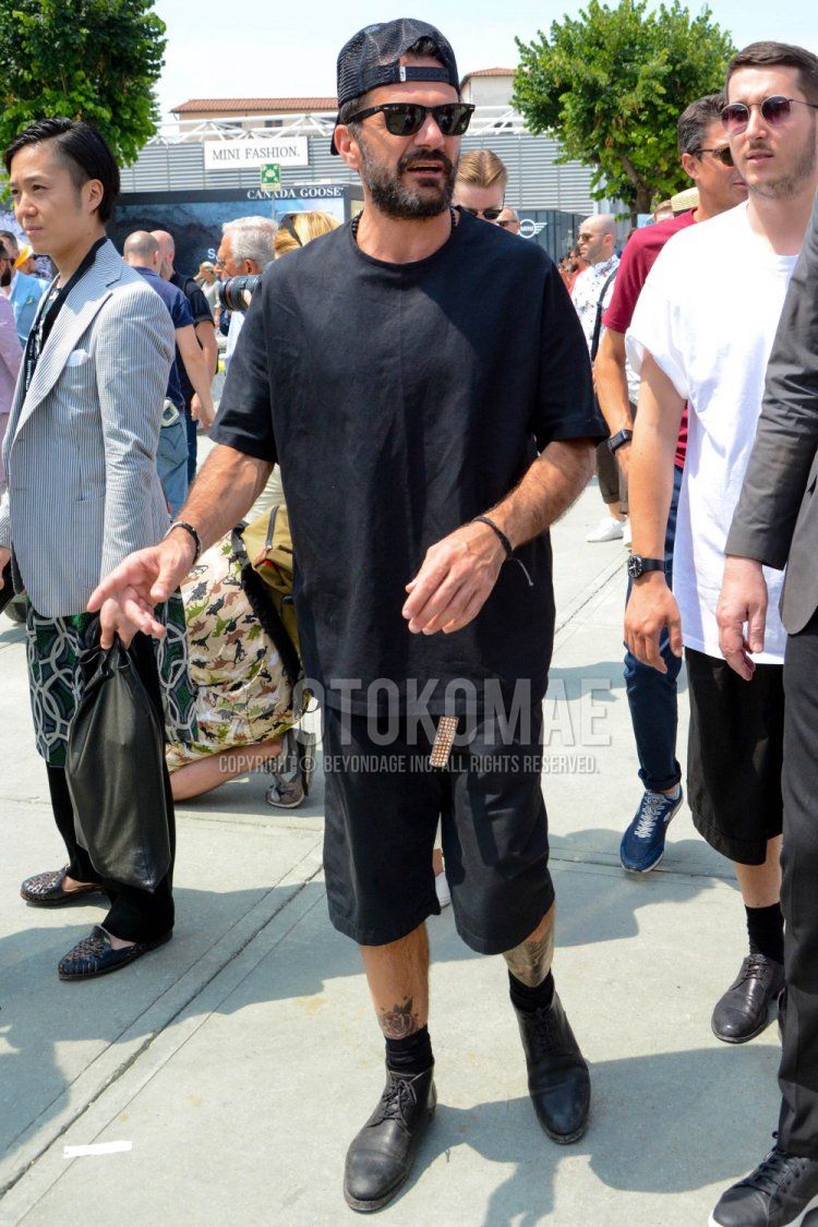 黒無地のベースボールキャップ、レイバン ウェイファーラー ウェリントンの黒無地のサングラス、黒無地のTシャツ、ブラウン無地のレザーベルト、黒無地のショートパンツ、黒無地のソックス、黒のブーツを合わせた春夏のメンズコーデ・着こなし。