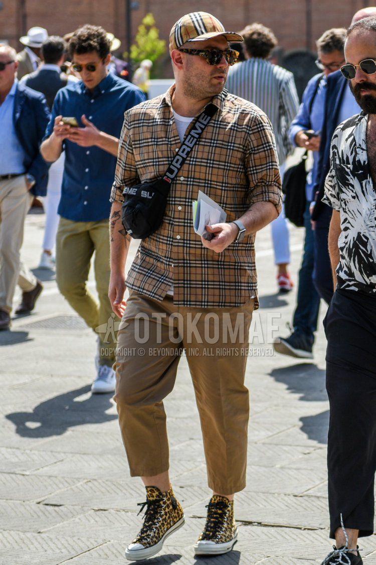 ベージュチェックのベースボールキャップ、黒べっ甲のサングラス、ブラウンチェックのシャツ、白無地のTシャツ、ブラウン無地のコットンパンツ、イエローハイカットのスニーカー、黒無地のボディバッグを合わせた春夏秋のメンズコーデ・着こなし。