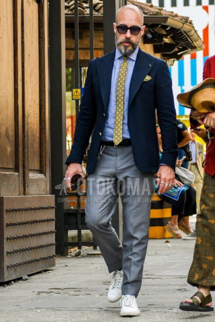 Men's spring/summer/fall outfit with plain sunglasses, plain navy tailored jacket, plain blue shirt, plain black leather belt, plain gray slacks, white sneakers, and yellow dot tie.