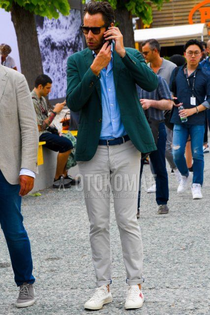 Men's spring, summer, and fall coordinate and outfit with Ray-Ban Wellington solid black sunglasses, solid green tailored jacket, solid blue shirt, solid navy leather belt, solid beige chinos, and Play Comme des Garcons Chuck Taylor white low-cut sneakers.