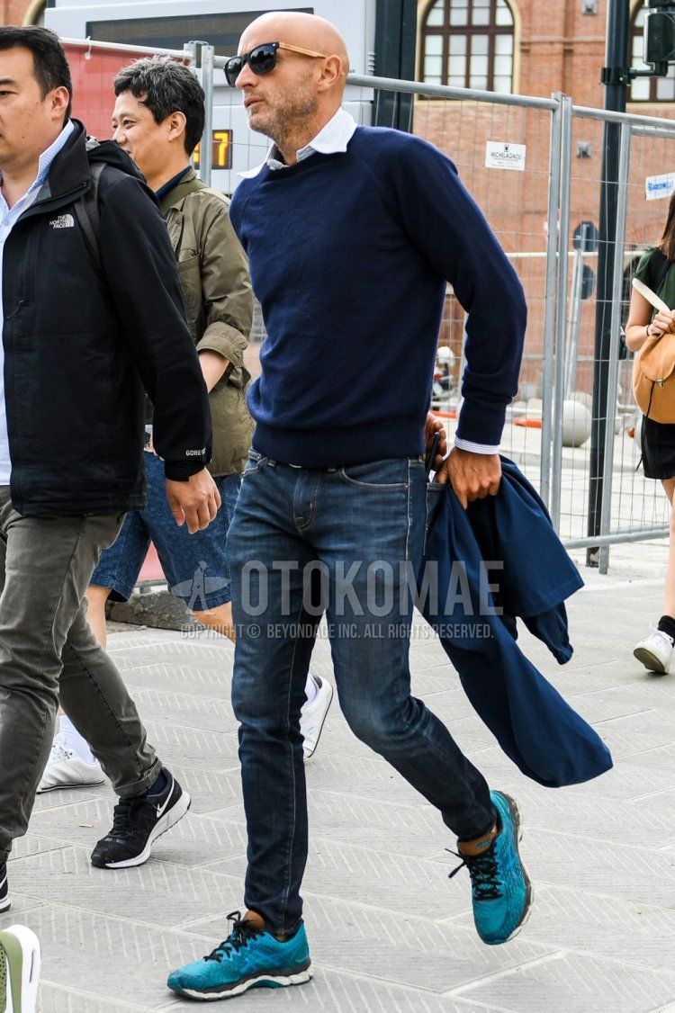 Men's spring/summer/fall coordinate/outfit with solid color sunglasses, solid color navy sweater, white/light blue striped shirt, solid color blue denim/jeans, and light blue low-cut sneakers.