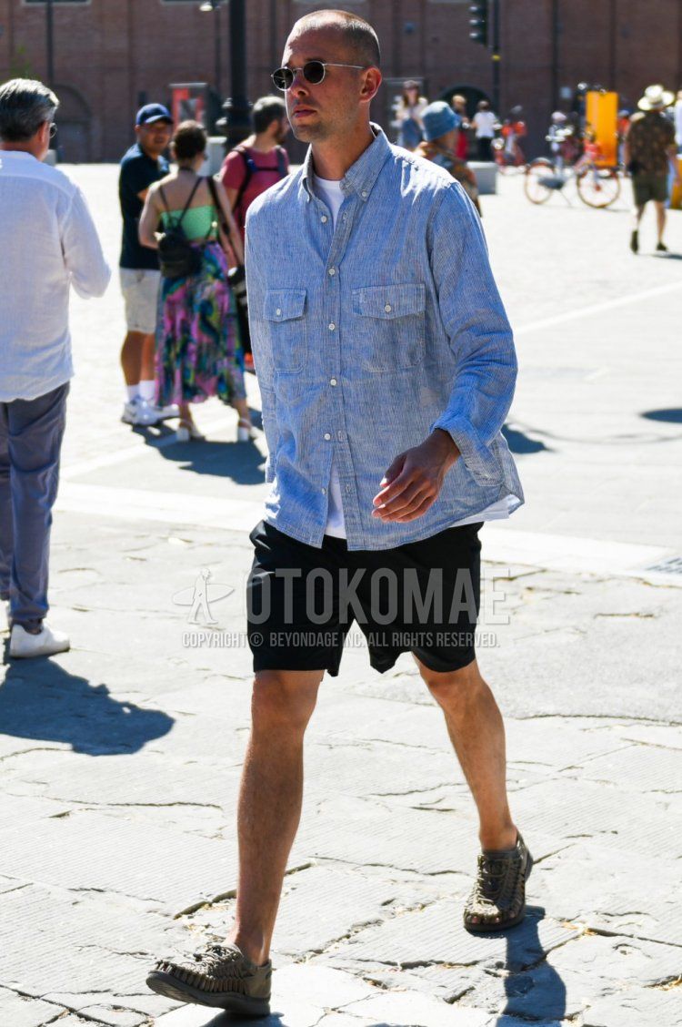 A summer men's coordinate and outfit with round black and silver solid sunglasses, gray striped denim/chambray shirt, solid white t-shirt, solid black shorts, and Keen olive green sport sandals.