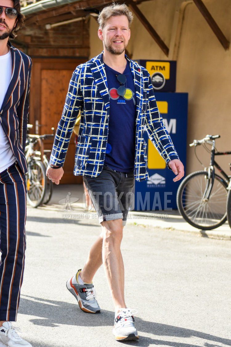 Spring, summer and fall men's coordinate and outfit with navy, yellow and white checked tailored jacket, navy graphic t-shirt, plain gray shorts and gray low-cut sneakers.