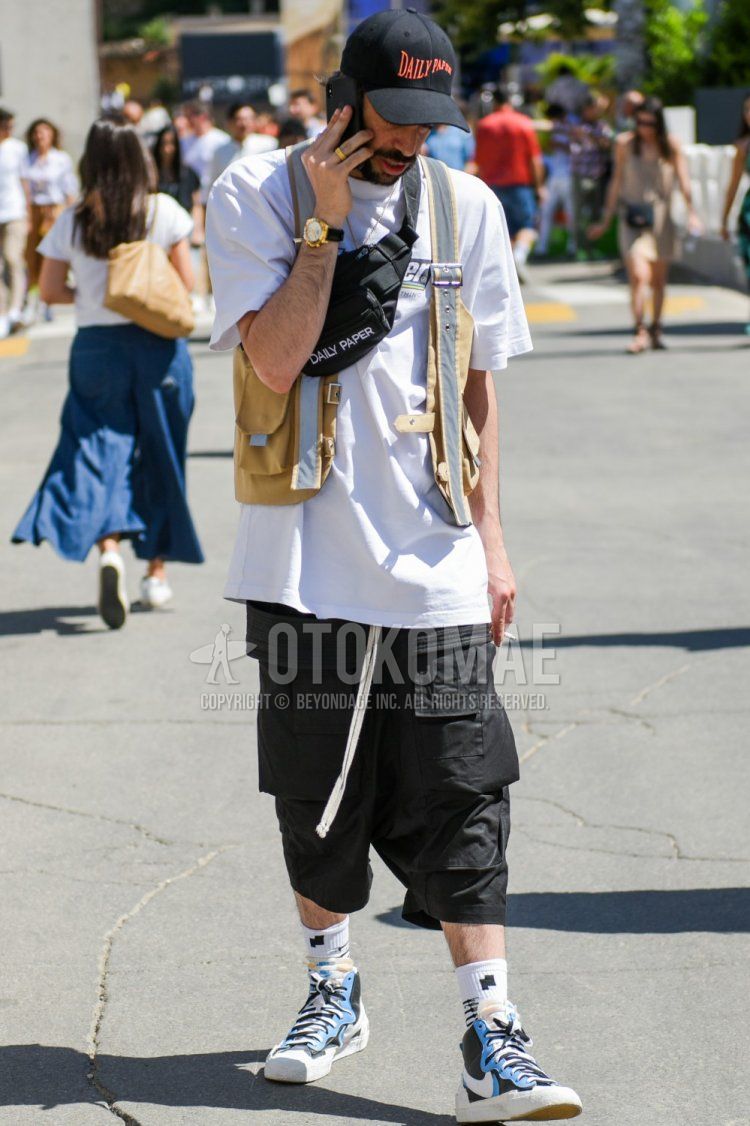 Summer men's summer coordinate with black graphic baseball cap, white graphic t-shirt, plain beige casual vest, plain black Rick Owens sarouel pants, white graphic socks, and Nike Sakai Blazer Mid white, light blue, and black high-cut sneakers. Outfit.