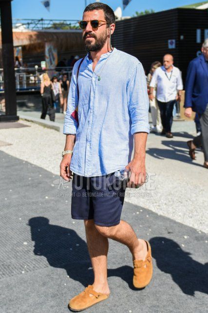 Summer men's coordinate and outfit with solid beige sunglasses, solid light blue shirt with band collar linen, solid navy chinos, solid shorts, and suede beige leather sandals.