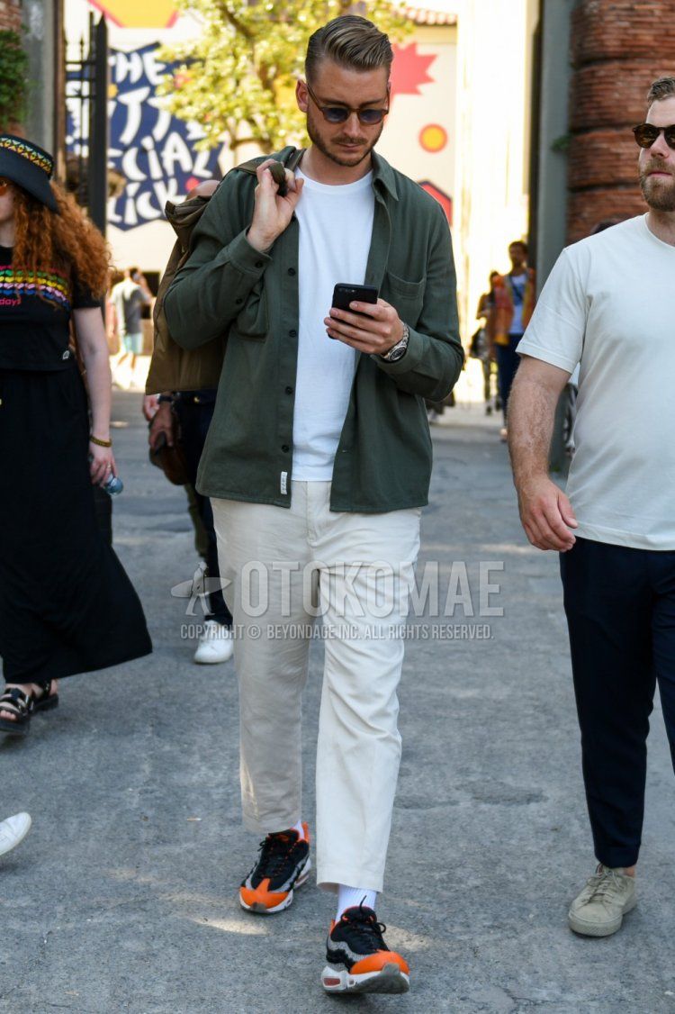 Spring and fall men's coordinate and outfit with plain brown sunglasses, plain olive green shirt jacket, plain white t-shirt, plain white cotton pants, plain white ankle pants, plain white socks, and Nike Air Max 95 orange and black low-cut sneakers.