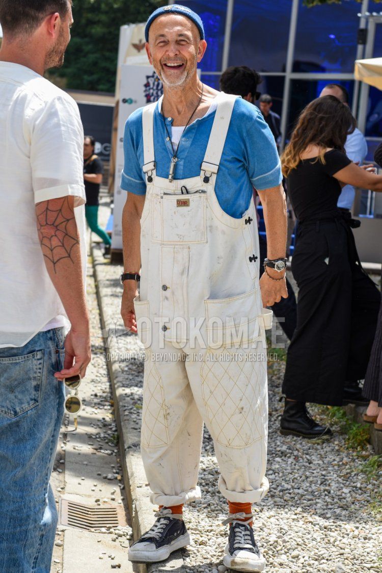 Men's spring, summer, and fall coordinate and outfit with plain blue knit cap, overallsf plain white jumpsuit, plain blue t-shirt with henley neck, plain red socks, and black low-cut sneakers.