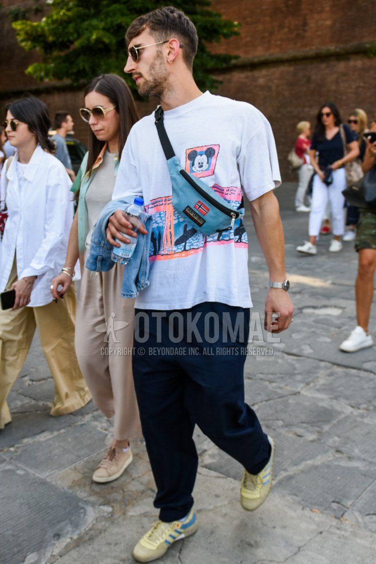 Summer men's coordinate and outfit with gold and black plain sunglasses, white graphic t-shirt, navy plain pleated pants, Adidas beige low-cut sneakers, and light blue one-pointed sacoche.
