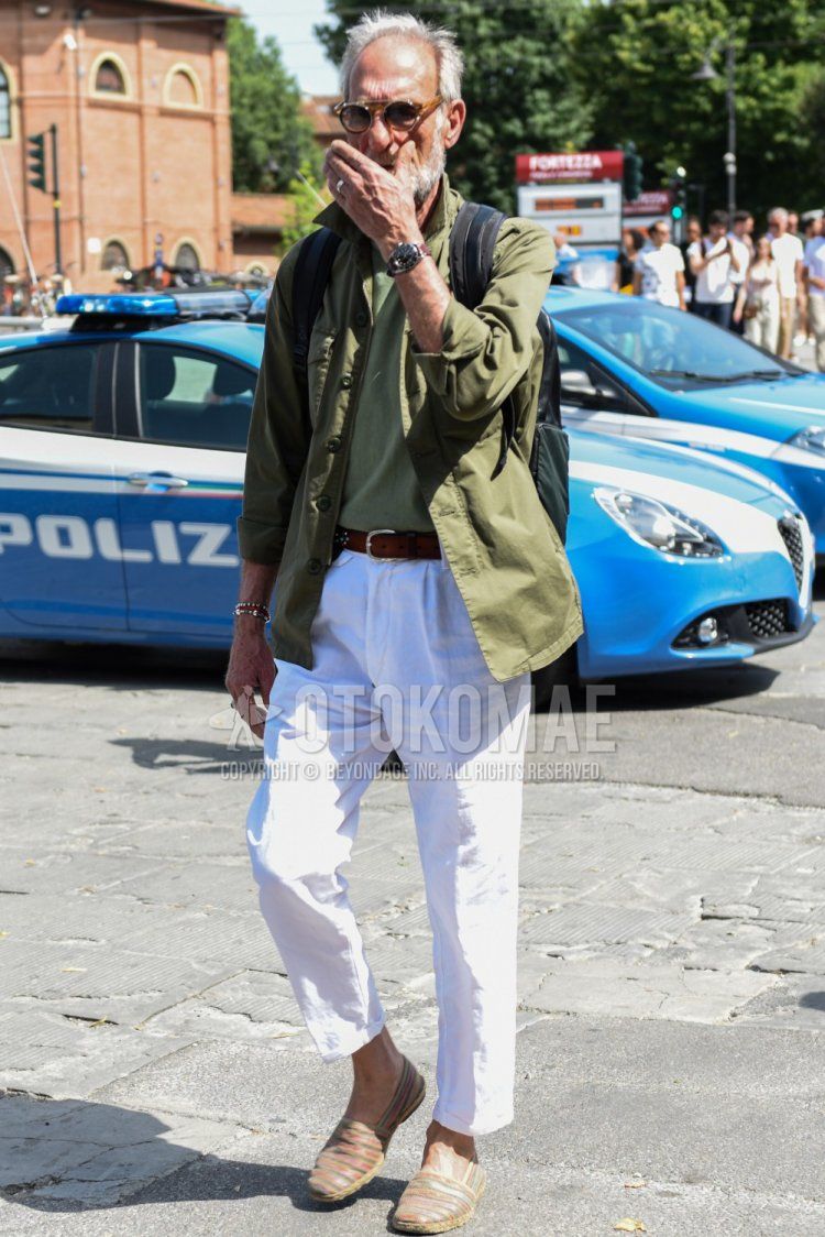 Men's spring/summer/fall outfit with plain brown sunglasses, plain olive green shirt jacket, plain olive green t-shirt, plain brown leather belt, plain white slacks, plain white ankle pants, and multi-colored striped espadrilles.