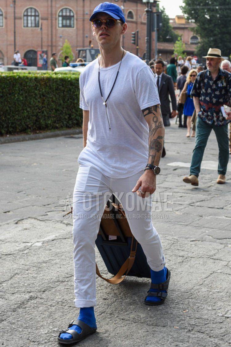Summer men's coordinate and outfit with plain blue baseball cap, plain brown sunglasses, plain white t-shirt, plain white cotton pants, plain blue socks, and gray leather sandals.