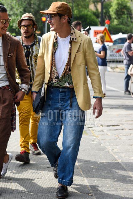 Men's spring/summer/autumn coordinate and outfit with plain brown baseball cap, plain black sunglasses, multi-colored graphic shirt, plain white t-shirt, plain blue wide pants, black coin loafer leather shoes, and plain navy clutch/second bag/drawstring bag.