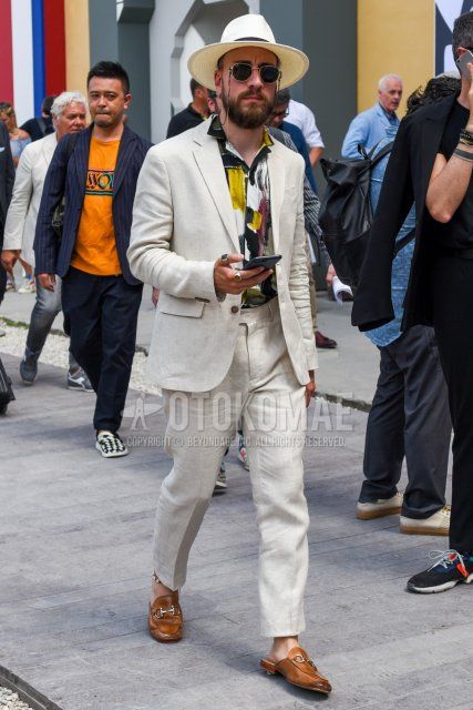 Men's spring/summer outfit/coordination with beige solid hat, Ray-Ban round black/gold solid sunglasses, black/yellow top/inner shirt, brown leather sandals, and beige solid suit.
