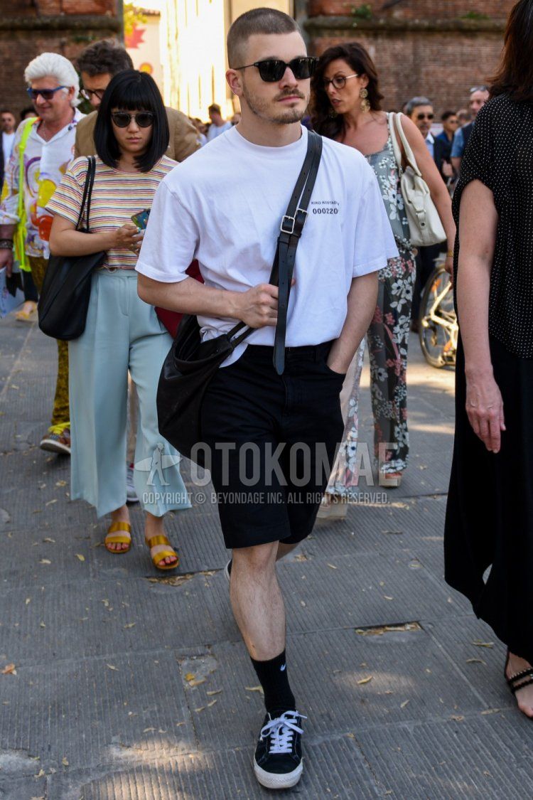 A summer men's coordinate and outfit with plain black sunglasses, Kiko Kostadinov one-pointed white T-shirt, plain black shorts, Nike one-pointed black socks, black low-cut sneakers, and a plain black shoulder bag.