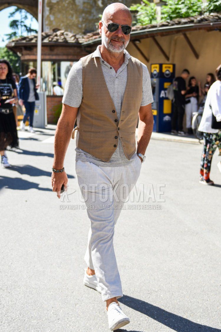 Teardrop Ray-Ban aviator black and silver solid sunglasses, solid beige gilet, solid gray polo shirt, solid gray slacks, and white low-cut sneakers for men in summer.