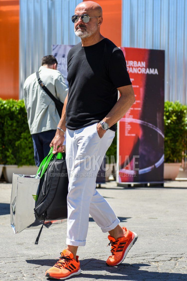 A summer men's coordinate and outfit with plain silver sunglasses, plain black t-shirt, plain white cotton pants, Adidas orange low-cut sneakers, and plain gray backpack.