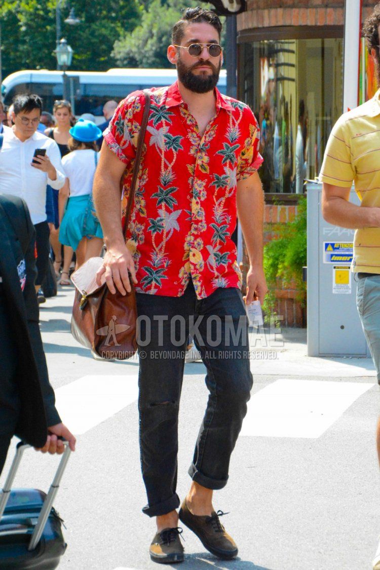 Men's spring/summer coordinate and outfit with gold solid color sunglasses, short sleeved red botanical shirt, dark gray solid color denim/jeans, brown low cut sneakers, brown solid color shoulder bag.