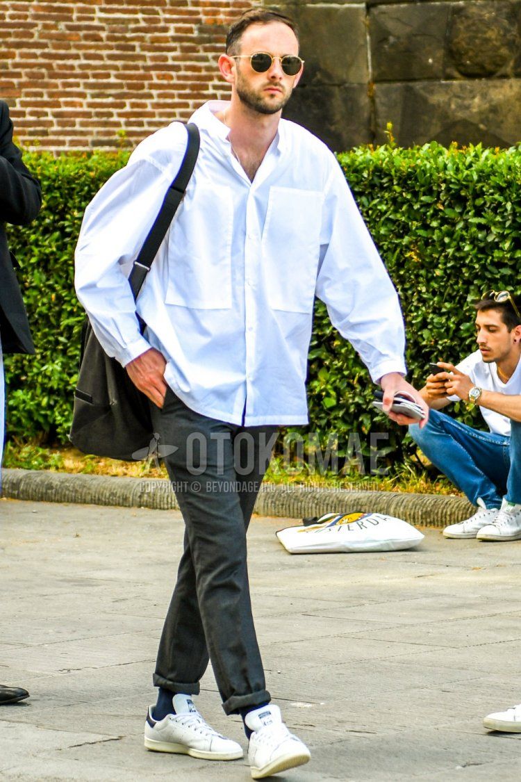 Men's summer coordinate and outfit with solid color sunglasses, solid color white shirt, solid color gray slacks, solid color navy socks, Adidas Stan Smith white low-cut sneakers, and solid color black shoulder bag.