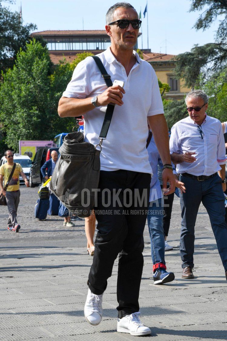 Men's spring/summer coordinate and outfit with plain black Ray-Ban sunglasses, plain white polo shirt, plain black denim/jeans, Adidas Stan Smith white low-cut sneakers, and plain gray shoulder bag.