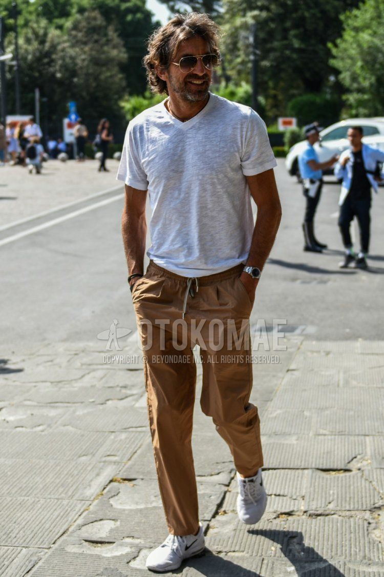 Summer men's coordinate and outfit with gold plain sunglasses, white plain t-shirt, brown plain easy pants, and white low-cut Nike sneakers.