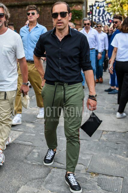 Men's spring and fall coordinate and outfit with solid color sunglasses, solid color black shirt, solid color green easy pants, and black low-cut sneakers.