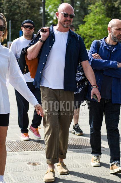 Summer men's coordinate and outfit with clear plain sunglasses, short-sleeved plain navy shirt, plain white t-shirt, plain beige chinos, and beige leather sandals.