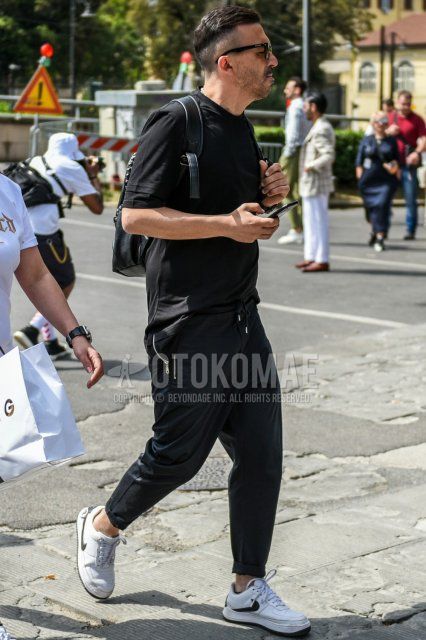 Men's summer coordinate and outfit with plain black sunglasses, plain black t-shirt, plain black easy pants, Nike white low-cut sneakers, and plain black backpack.