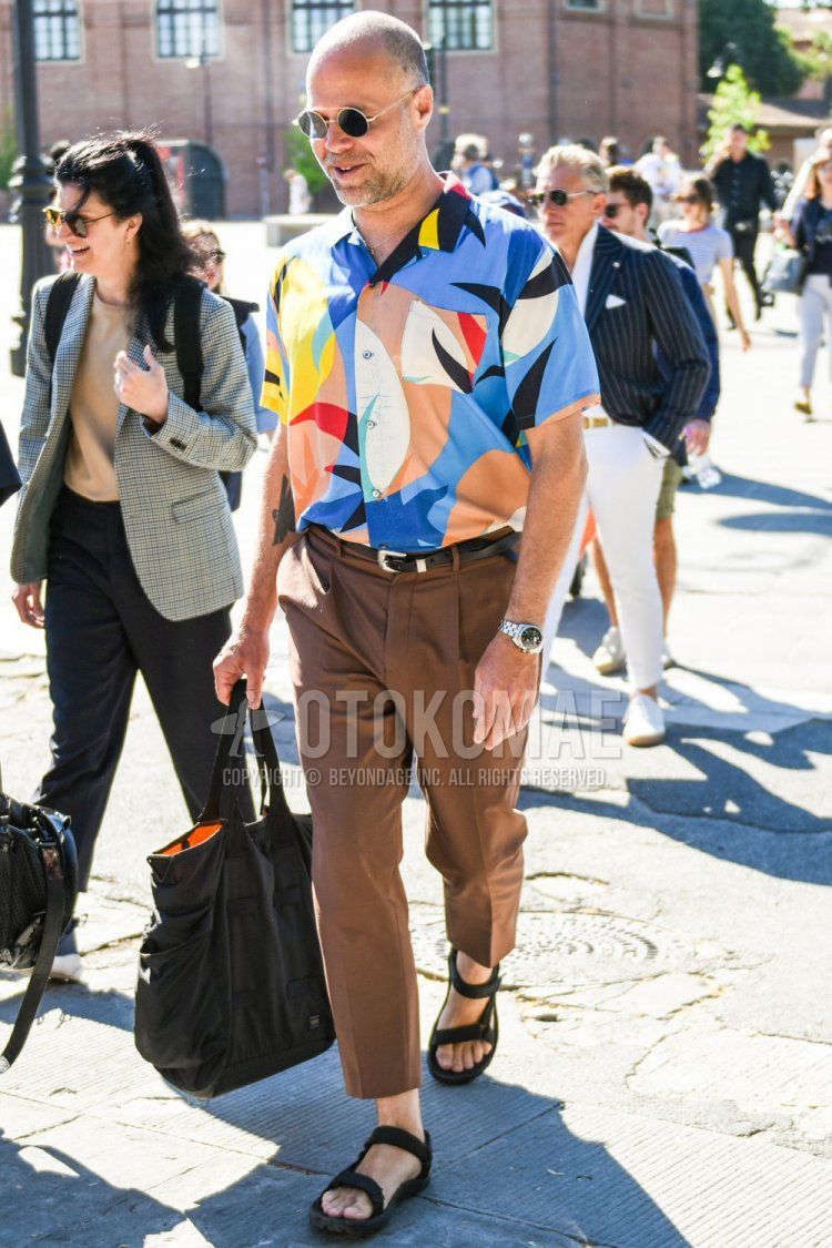 Summer men's coordinate and outfit with plain gold sunglasses, open-colored multi-colored top/inner shirt, plain black leather belt, plain brown ankle pants, black sport sandals, and plain black Porter tote bag.
