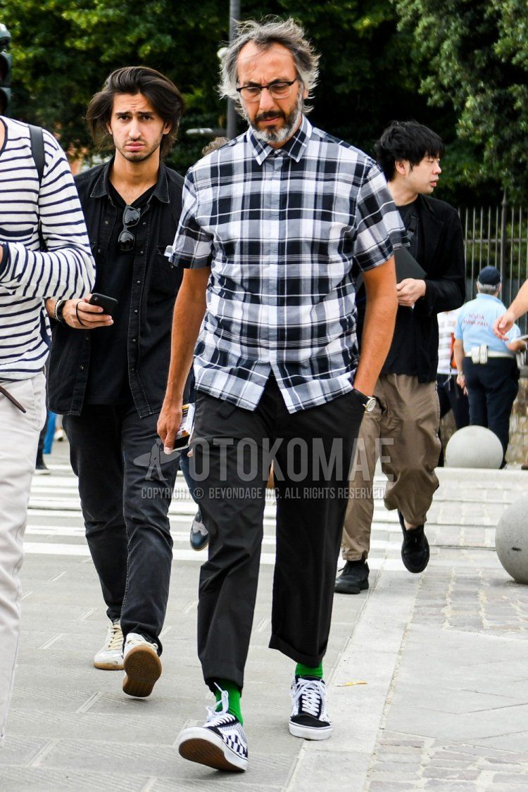 Men's summer coordinate and outfit with plain glasses, black/white checked shirt, plain black ankle pants, plain black slacks, plain green socks, and black low-cut sneakers by Vans.