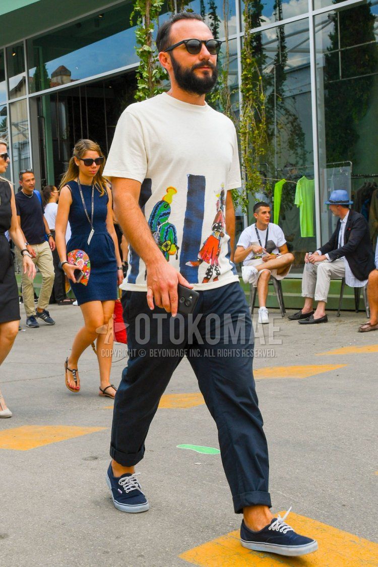 Men's spring/summer coordinate and outfit with plain black sunglasses, beige graphic t-shirt, plain navy chinos, and navy low-cut sneakers from Vans.
