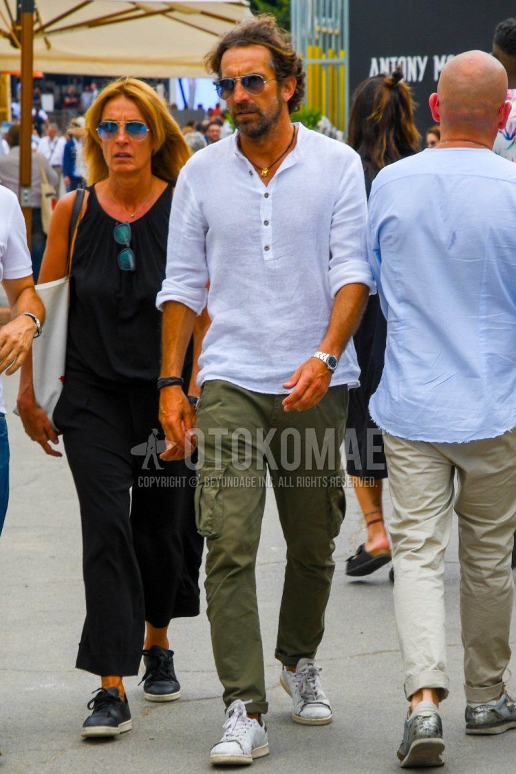 Men's summer coordinate and outfit with Ray-Ban teardrop brown/silver solid color sunglasses, plain white shirt with henley neck, olive green solid color cargo pants, and Adidas Stan Smith white low-cut sneakers.