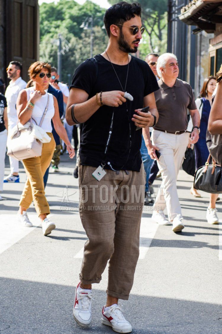 Men's spring/summer coordinate and outfit with round gold plain sunglasses, plain black t-shirt, linen brown plain slacks, and white low-cut sneakers by Diadora.