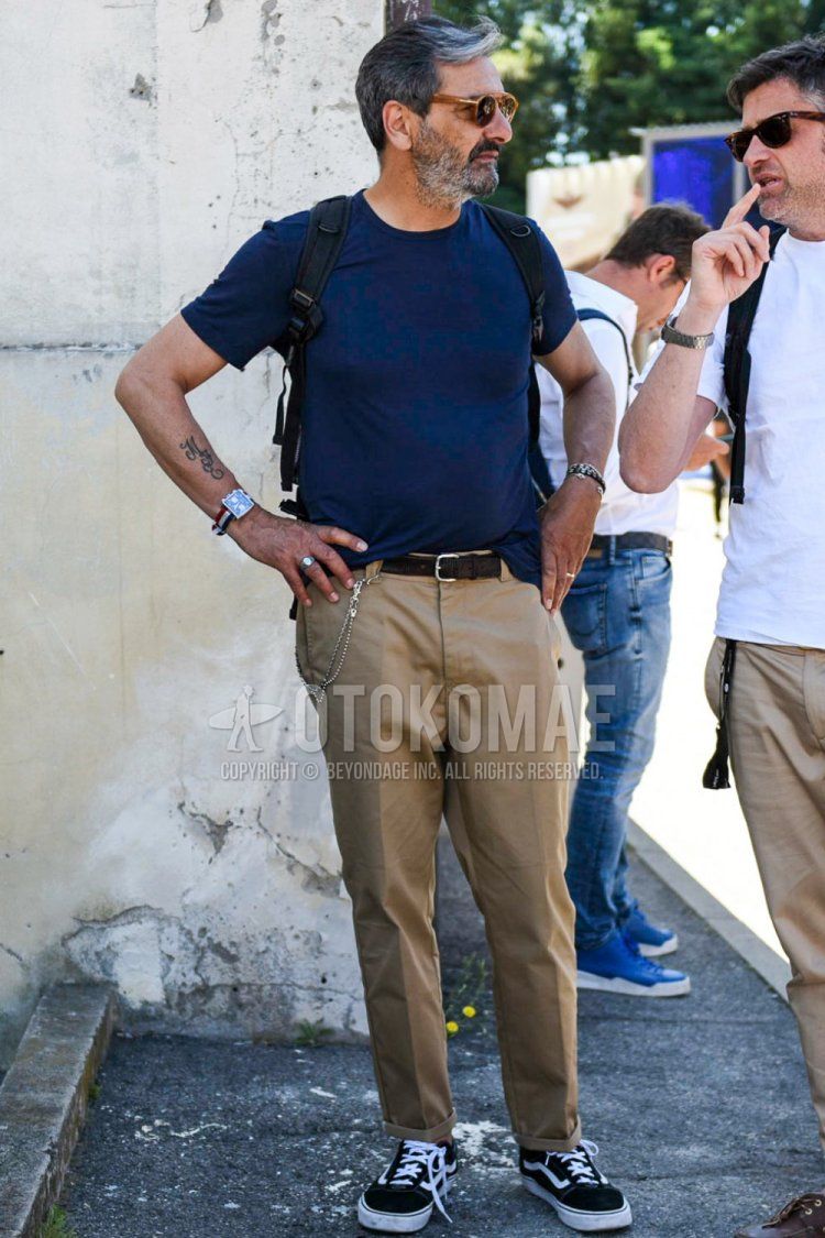 Summer men's coordinate and outfit with solid beige sunglasses, solid navy t-shirt, solid brown leather belt, solid beige chinos and Old School Vans black low-cut sneakers.