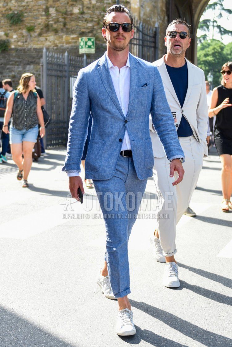 Men's spring, summer, and fall coordination and outfit with plain black sunglasses, plain white shirt, plain black leather belt, white low-cut sneakers, and plain blue suit.