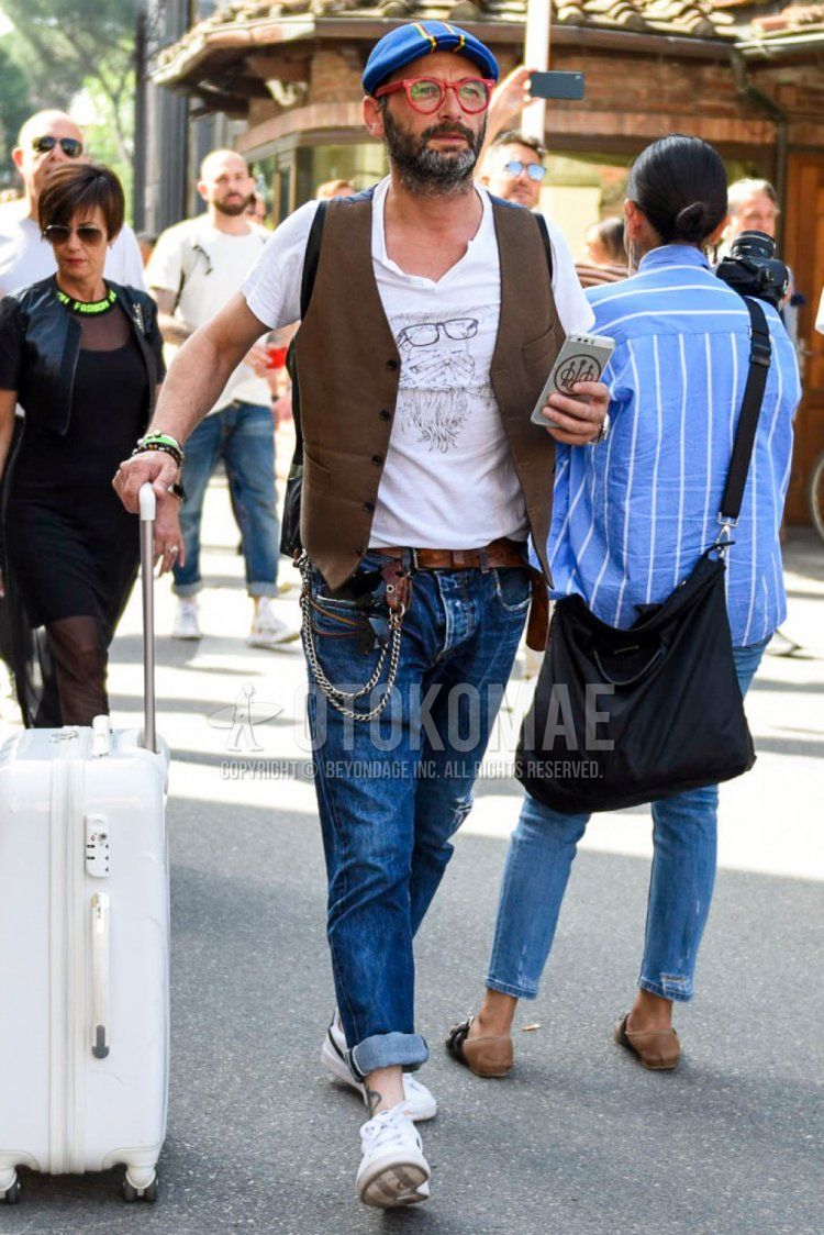 Summer men's coordinate and outfit with blue cap hat, red solid color glasses, brown solid color gilet, white graphic t-shirt, brown solid color leather belt, blue solid color damaged jeans and white low cut sneakers.