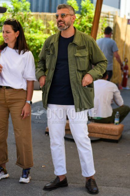 Men's spring and fall outfit with round gold solid sunglasses, olive green solid shirt jacket, olive green solid safari jacket, black solid t-shirt, white solid cotton pants, white solid ankle pants, and black coin loafer leather shoes.
