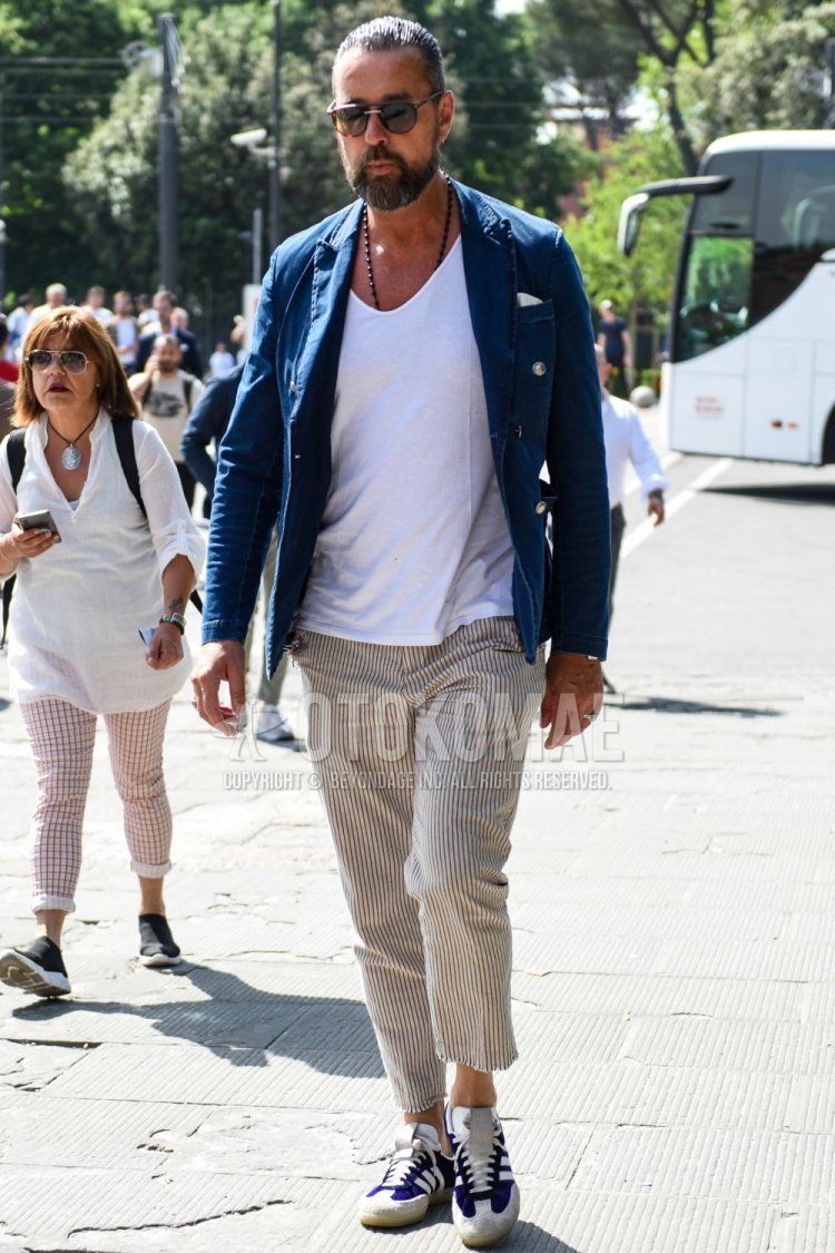 Men's spring, summer, and fall coordinate and outfit with brown tortoiseshell sunglasses, plain blue tailored jacket, plain white t-shirt, beige/brown striped ankle pants, and white/purple low-cut sneakers.
