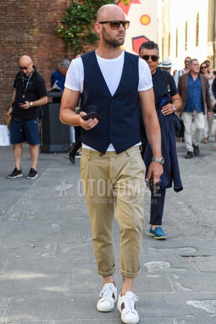 Men's summer coordinate and outfit with plain black sunglasses, plain white T-shirt, plain navy gilet, plain beige chinos and white low-cut sneakers.