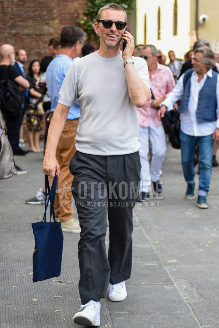 A summer men's outfit and outfit with Wayfarer plain black sunglasses, knit plain beige t-shirt, plain gray slacks, white high-cut sneakers, and plain navy tote bag.