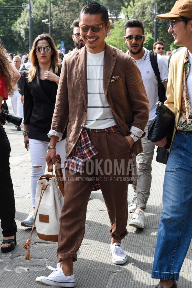 Men's spring, summer, and fall coordination and outfit with plain brown sunglasses from Boston, white striped t-shirt, white low-cut sneakers, plain white/beige shoulder bag, and plain brown suit.
