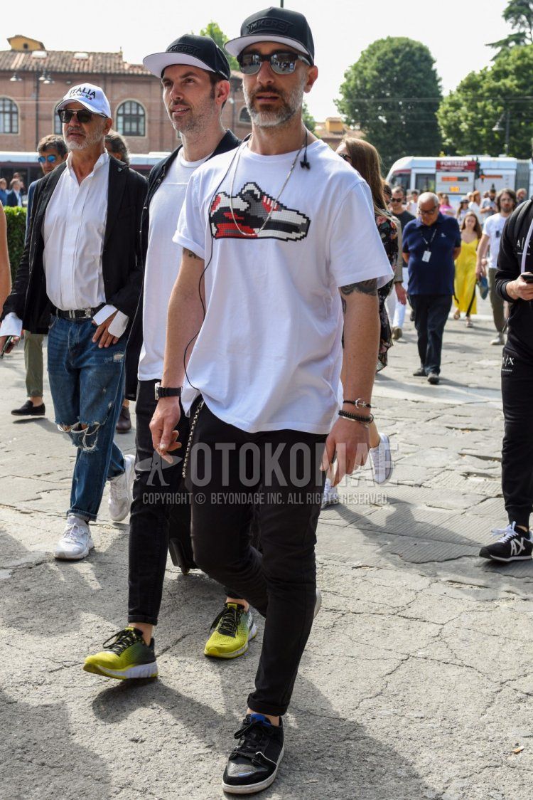 Summer men's coordinate and outfit with plain black baseball cap, plain black sunglasses, mostly heard rarely seen white graphic t-shirt, plain black cotton pants, and black low-cut sneakers.