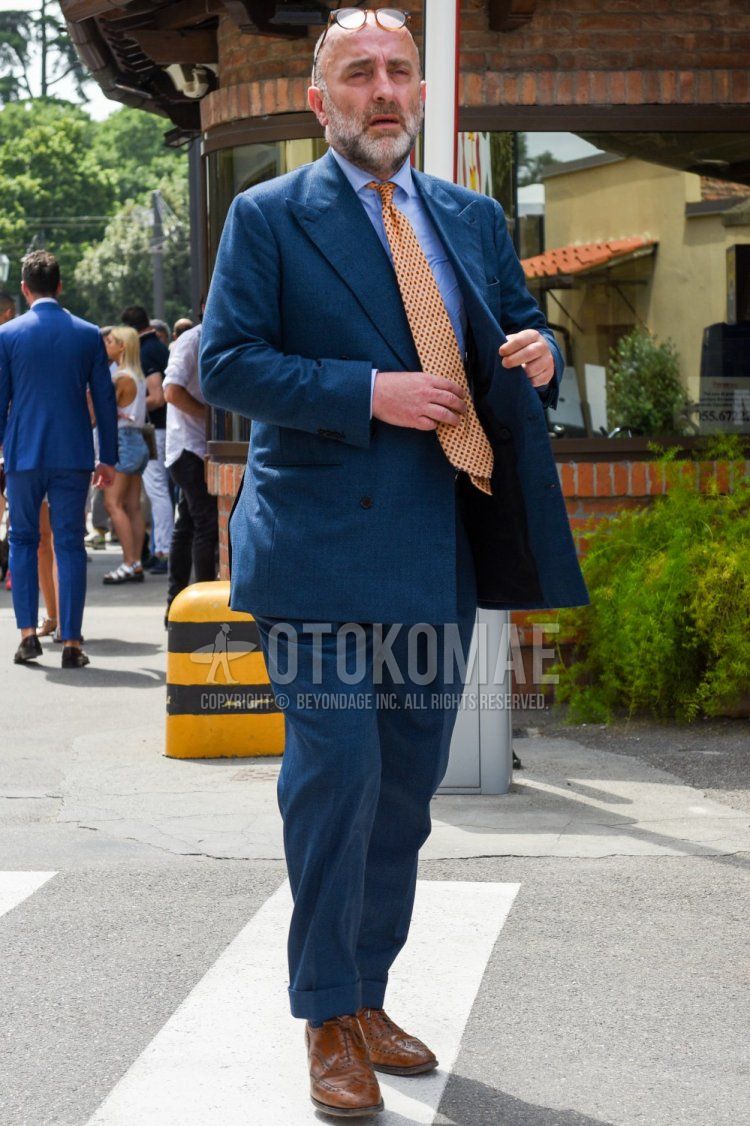 Men's spring, summer, and fall coordination and outfit with plain light blue shirt, brown brogue shoes leather shoes, plain blue suit, and orange dot tie.