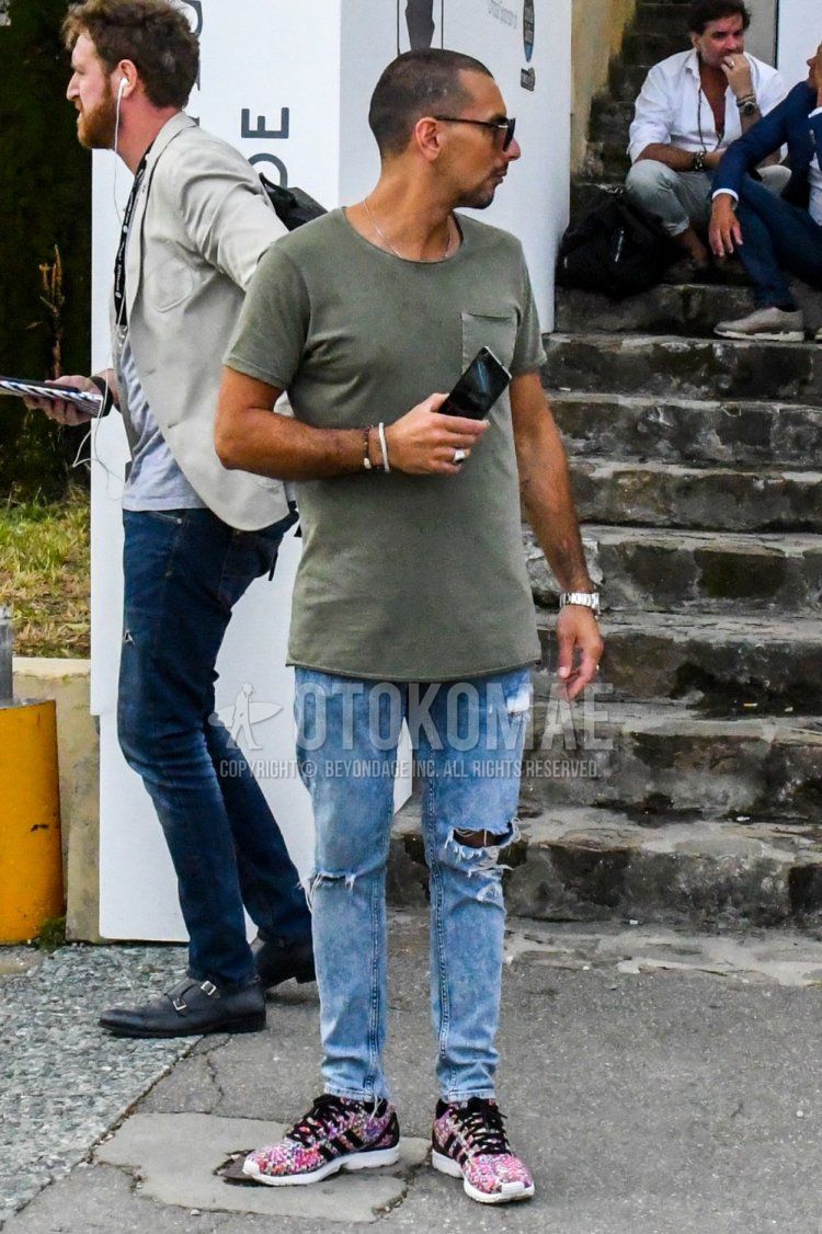 Men's spring and summer coordinate and outfit with plain sunglasses, plain olive green t-shirt, plain blue damaged jeans, and Adidas pink multi-colored low-cut sneakers.