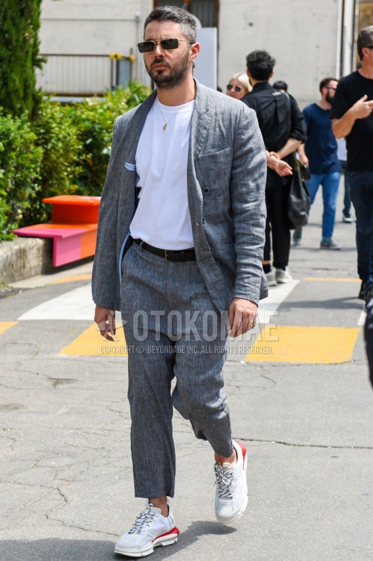 Men's spring, summer, and fall coordination and outfit with square gold and solid black sunglasses, solid white t-shirt, solid black leather belt, white low-cut sneakers, and solid gray suit.