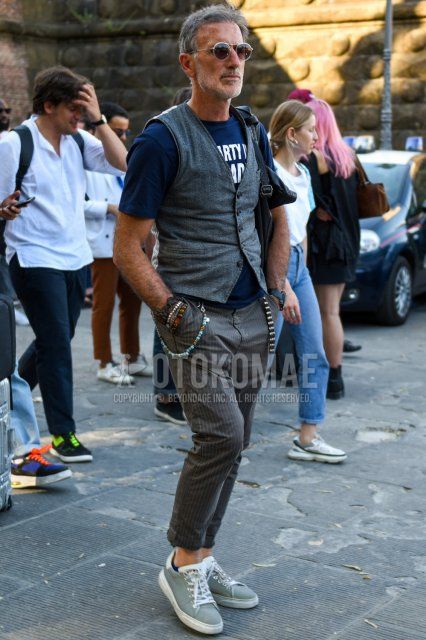 シルバー・ブラウン無地のサングラス、グレー無地のジレ、ダークグレーグラフィックのTシャツ、グレーストライプのスラックス、グレーローカットのスニーカーを合わせた春夏のメンズコーデ・着こなし。