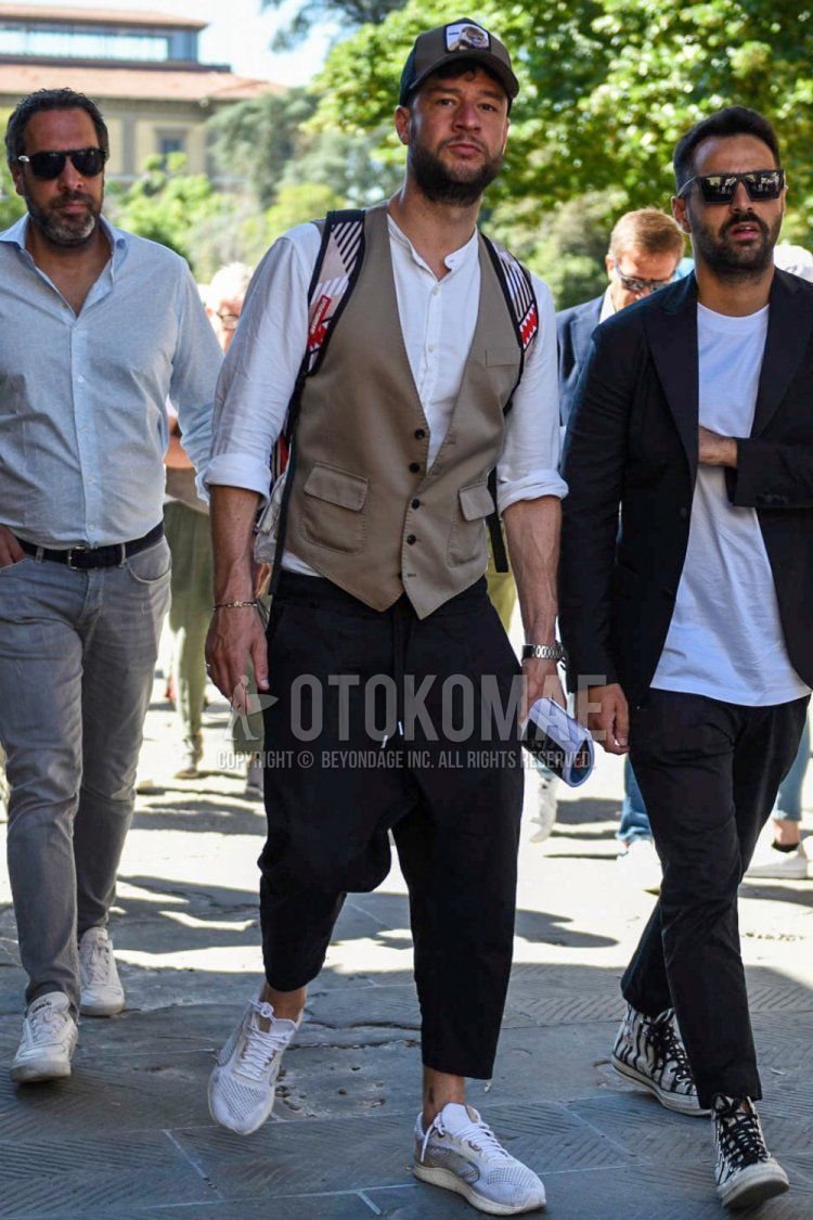 Men's spring/summer coordinate and outfit with beige graphic baseball cap, solid beige gilet, solid white shirt with band collar, solid black easy pants, solid cropped pants, solid pleated pants, and white low-cut sneakers.